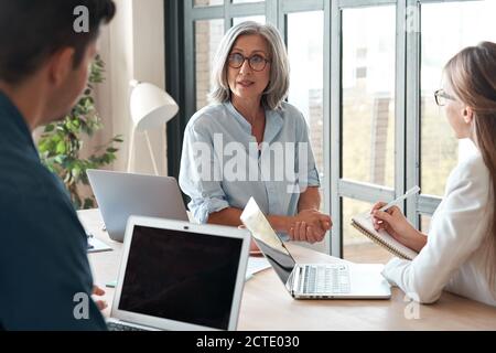 Old female mentor supervisor training young interns at group office meeting. Stock Photo