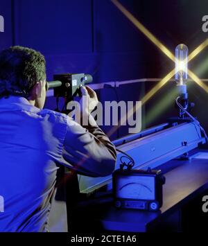 Pictured is a method for testing high temperature measurements by comparing the color spectrum of light at various power settings with an Optical Pyrometer.  The devices are calibrated at NIST.  The power through the bulb is varied and monitored by the meter on the table.  The scanning device that the technician is looking though is adjusted till the color scheme viewed within in the device matches the color of the emanating from the bulb at the particular power setting.  Using a relationship table provided, the technicians can then identify the temperature.  The light source pictured is used Stock Photo