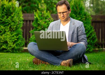 Adult smart businessman works on laptop outdoors, online traiding, e-commerce Stock Photo