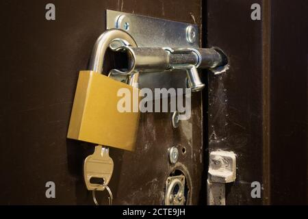 Padlock and bolt on heavy damaged door. Emergency fix after robbers burglarized a building twice in 2 days. Emergency exit door bolted from the inside Stock Photo