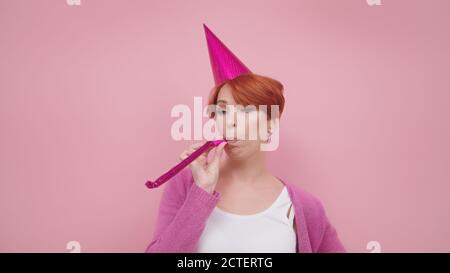 Bored red haired middle aged woman blowing party horn on the birthday party. Purple colors. High quality photo Stock Photo
