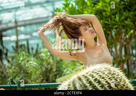 Pretty young woman standing near the cactus and holding her hair Stock Photo