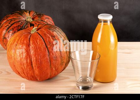 two pumpkins and a bottle of pumpkin juice on a wooden table. empty juice glass. dark grey background. pumpkin juice concept Stock Photo