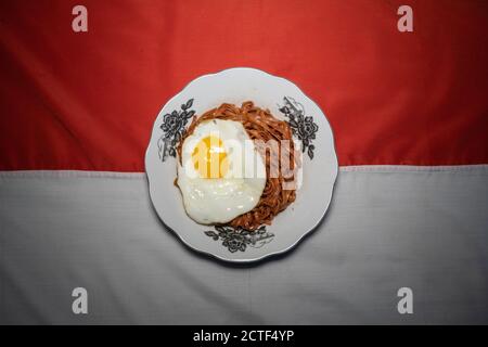 Fried instant noodles are enjoyed with fried eggs on a plate with a typical Indonesian ethnic cloth ornament Stock Photo