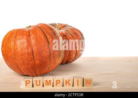 two pumpkins on a wooden table. the word PUMPKIN is laid out in wooden cubes. agriculture pamkin concept. white background Stock Photo