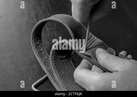 A man makes holes in a leather collar with an awl. Hands of an adult man with a metal awl and a wide collar. Pet equipment repair. Selective focus. Stock Photo