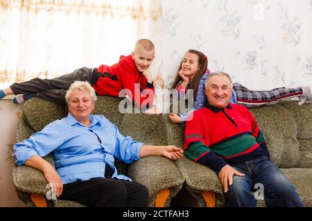 Grandchildren jumping on couch with their grandparents in the living room Stock Photo