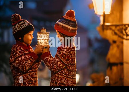 Beautiful children, boy brothers holding lantern, casually dressed, looking at night view of Prague city, wintertime Stock Photo