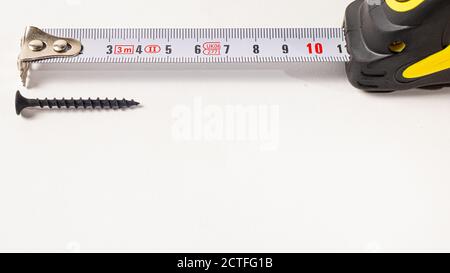 Measuring roulette yellow black and self-tapping screw on a white background banner with space for text. A construction tool tape measure. Stock Photo