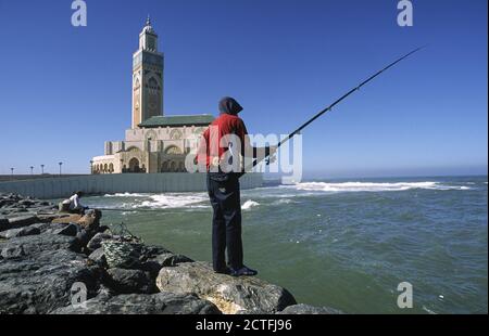 07.11.2010, Casablanca, Morocco, Africa - Two men fish under a blue sky at the shore in front of the Hassan II Mosque, the second largest mosque. Stock Photo