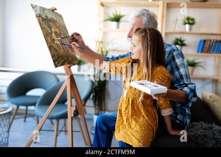 Senior man with child painting on canvas. Grandfather spending happy time with granddaughter. Stock Photo