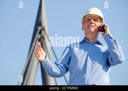 Architect or engineer talking on smart phone in front of an industrial building with blue sky - selective focus on the head Stock Photo
