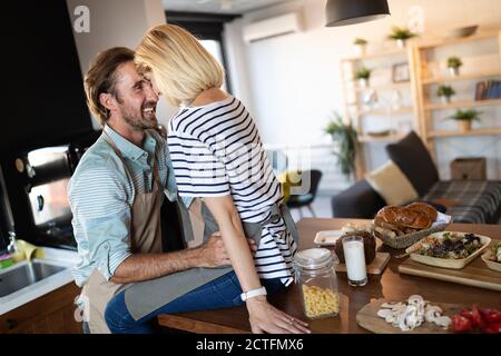 Beautiful young couple is talking and smiling while cooking healthy food in kitchen at home Stock Photo