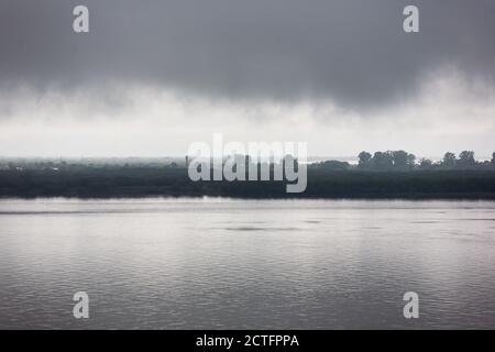 Summer thunderous landscape with river, forest and dark dramatic clouds. Stock Photo