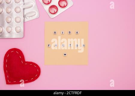 Concept of health, cardiology, heart disease. Words RISK FACTOR on white cubes, tablets in blisters on a pink background. Flat lay. Stock Photo