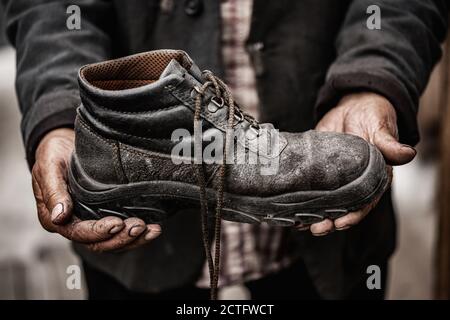 Homeless man holds old dirty boot with his hands. Shoe repair, poverty concept Stock Photo