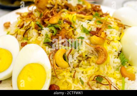Closeup of chicken biryani plate with cut eggs in the foreground with fried onions and cashew nuts spread on Stock Photo