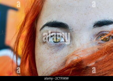 Close up portrait of a red hair woman girl with freckles. Portrait of a girl outdoors in sunlight. Hair covers half of the face.