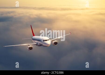 Airplane is flying above the clouds at sunset in summer
