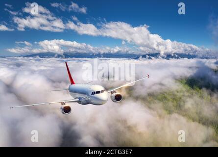 Airplane is flying in low clouds over mountains at sunset