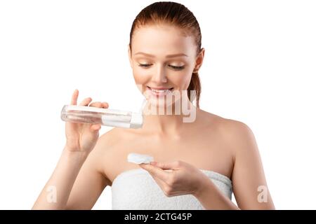 Red-Haired Millennial Woman Using Lotion And Cotton Pad, White Background Stock Photo