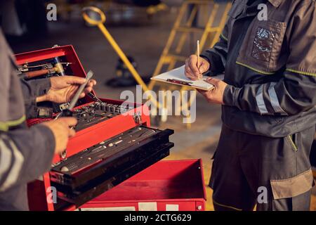Cropped head portrait of men aircraft with tools in hand and another male doing notes on the clipboard Stock Photo