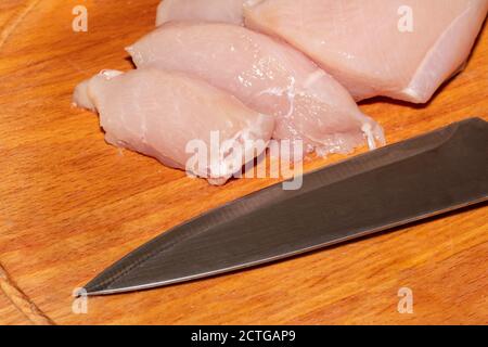 A high angle close-up shot of chicken pieces and a knife on a wooden board. Stock Photo