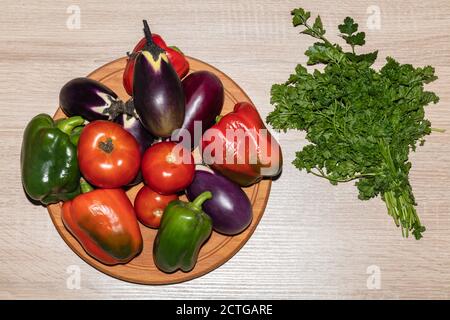 A top close-up shot of various vegetables like tomatoes, parsley, peppers, eggplants lying on a wooden cooking board. Isolated on wooden background. Stock Photo
