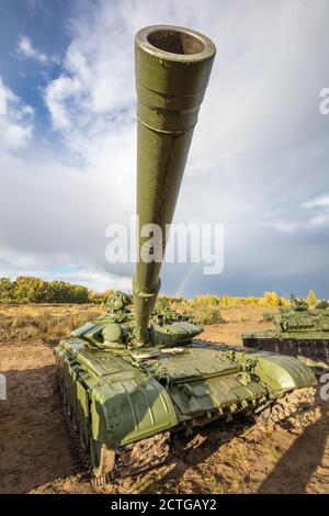 A high angle shot of russian tank T-64 in the field. Cannon pointing upwards straight in the camera. Blue cloudy sky as a background. Stock Photo