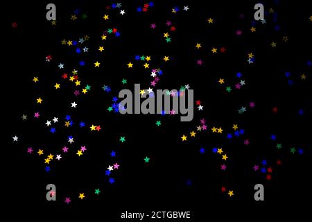 Multi-colored stars on a black background. Festive background of colorful confetti stars on a black background. Stock Photo