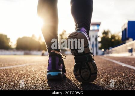 Runner feet running on stadium tracks closeup on shoe. Woman fitness sunset jog workout welness concept. Stock Photo