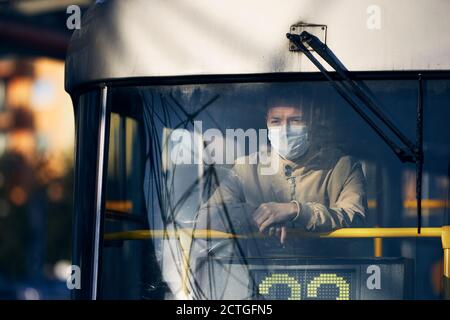 Man wearing face mask and looking from window of tram. Themes public transportation in new normal, coronavirus and personal protection. Stock Photo