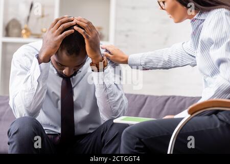 selective focus of psychologist calming frustrated african american man holding hands on head in hospital Stock Photo