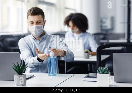 Rules for safety health during coronavirus outbreak. Man in protective mask treat his hands with antiseptic at workplace with laptop Stock Photo