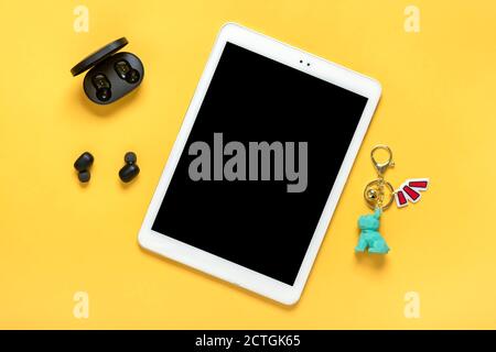 Tablet with black screen and wireless headphones, charger capsule on yellow background Mock up Flat lay Top view Social media, digital marketing Stock Photo