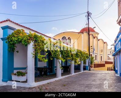 Pigadia, Karpathos, Greece - October 4, 2019: Early morning shot of quiet Apodimon Karpathion street in Pigadia town with church and restaurant Stock Photo
