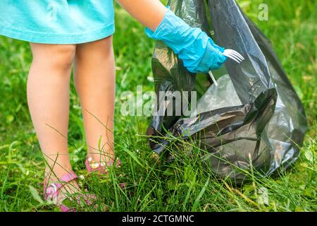 Child collects plastic trash from grass throwing garbage in garbage bag in the park Stock Photo