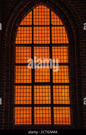Deep orange light coming from a church 's Gothic window conveys a diabolic, hellish and evil feeling with wicked, cruel and bad concept. Powerful and Stock Photo