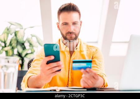 Shot of man holding credit card and mobile phone in his hands while paying bills with credit card. Stock Photo