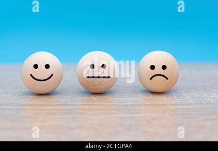 Three wooden faces with emotions: smile - happy, serious - neutral and angry - displeased, concept picture Stock Photo