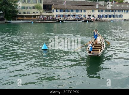 A Swiss fisherman traditional wooden boat with one small boy and woman. They are standing and move the vessel with oars on the Limmat river in Zurich. Stock Photo