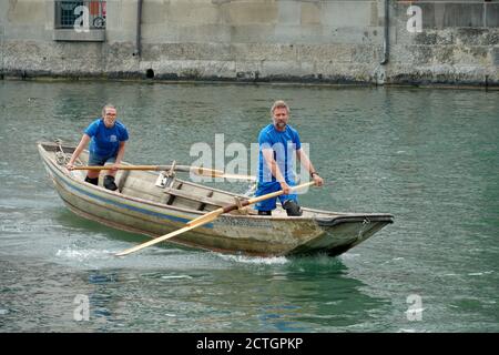 A Swiss fisherman traditional wooden boat with two crewmembers. They are standing and move the vessel with oars on the Limmat river in Zurich old city. Stock Photo