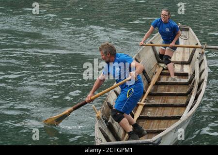 Man and women in a Swiss fisherman traditional wooden boat on sport event. They are standing and move the vessel with oars on the Limmat river. Stock Photo