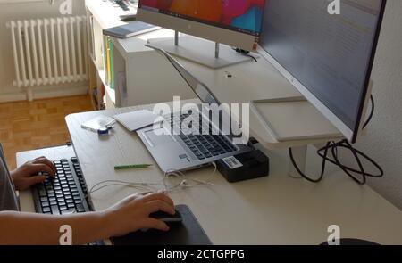 A woman in home office during coronavirus typing on a keyboard with one hand and using a mouse with the other. Using two monitors. Stock Photo