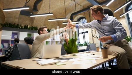 Celebrating success. Happy multiracial business people giving high five to each other and smiling while working together in the modern coworking space. Teamwork and collaboration Stock Photo