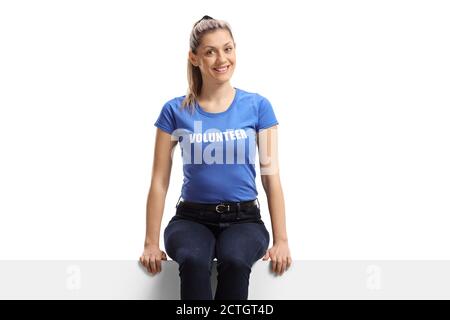 Young woman volunteer smiling and sitting on a white panel isolated on white background Stock Photo