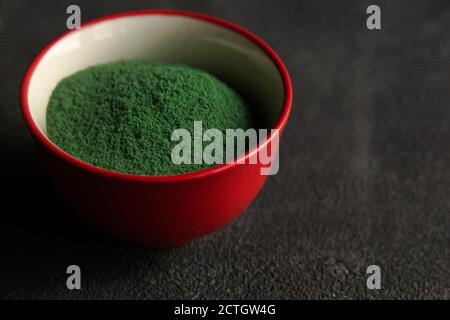 red bowl with Heap of green chlorella or spirulina algae, or matcha, on gray concrete background. Superfood concept powder. Space for text. Stock Photo