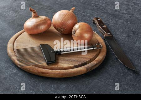 Onion cutting holder on cutting board, three  onions and kitchen knife Stock Photo
