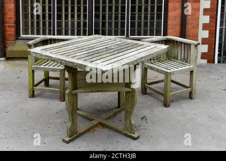 Isolated rustic wooden table and chairs outside building on concrete patio in summer Stock Photo