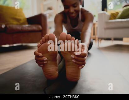 Closeup of healthy young woman touching feet while doing stretching exercise at home Stock Photo